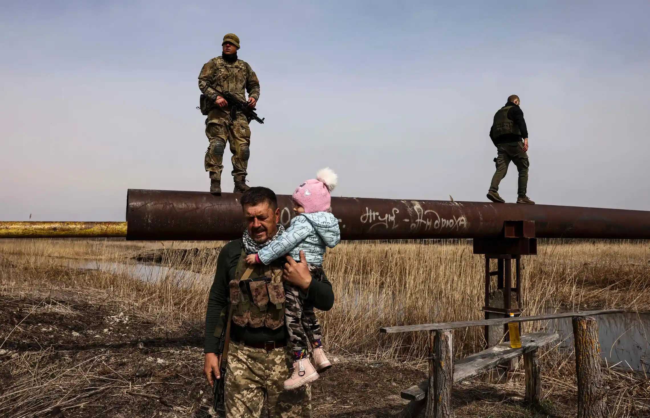 A Ukrainian serviceman carries the baby of a displaced family to help to cross a river, on the outskirts of Kyiv, on March 31, 2022